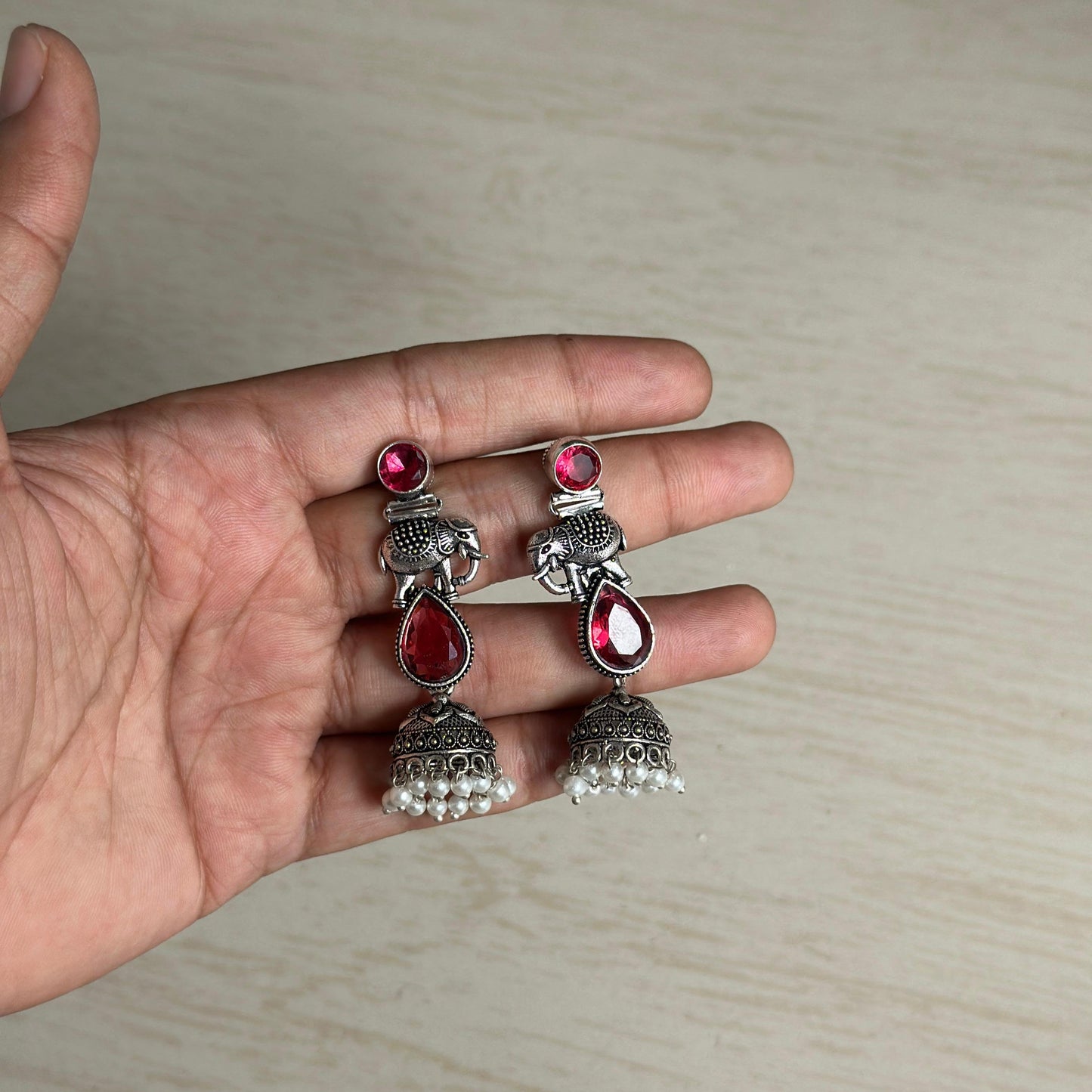 Oxidized jhumka earrings with elephant motif and red stone accents.