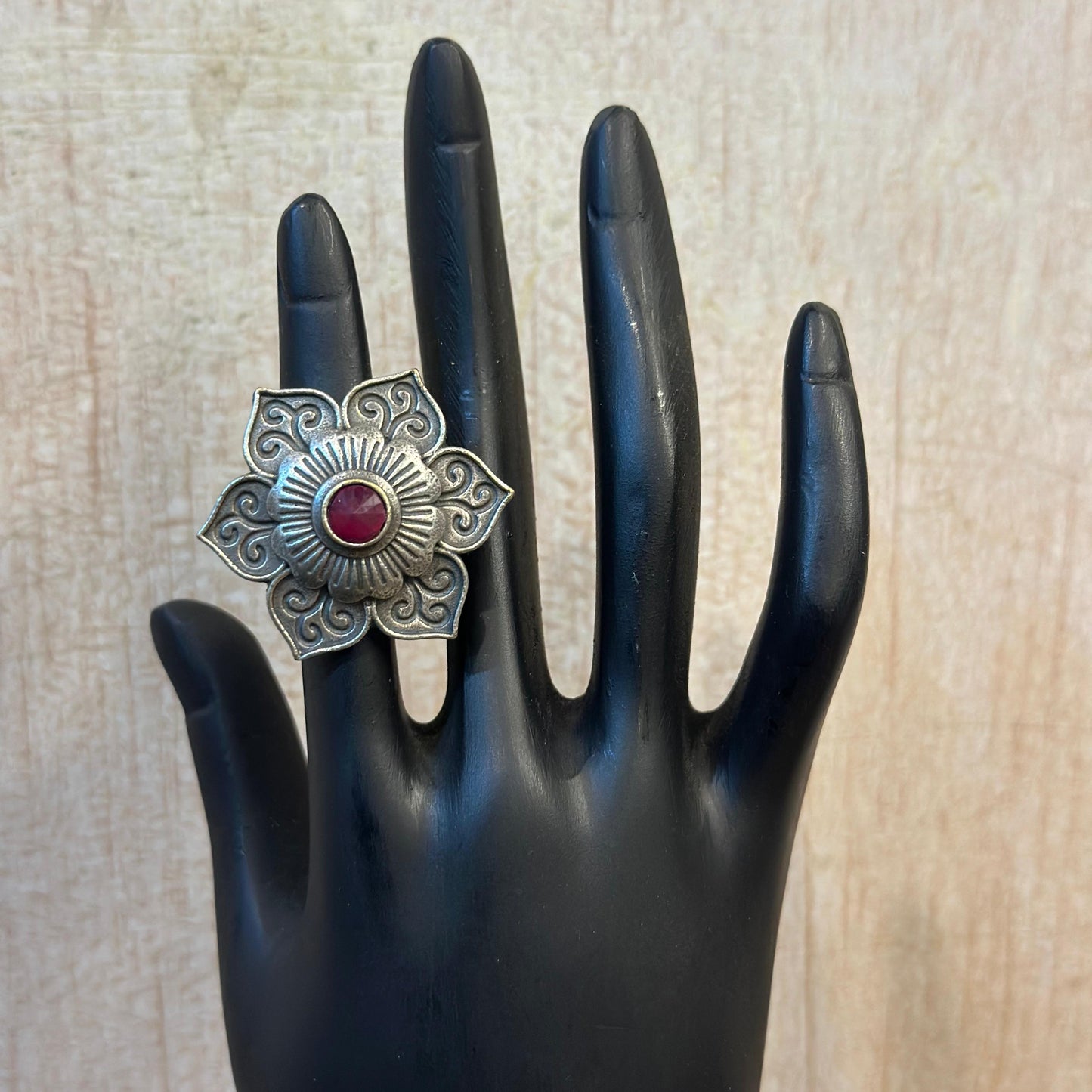 Oxidised silver floral ring with intricate design and red stone centerpiece.
