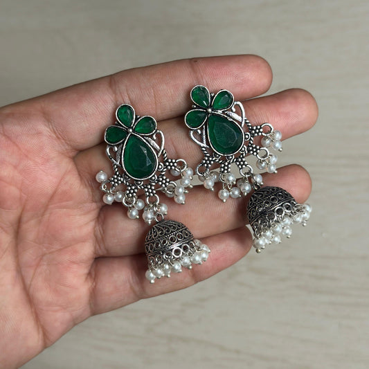 Oxidized jhumka earrings with green stone floral design and pearl bead detailing.