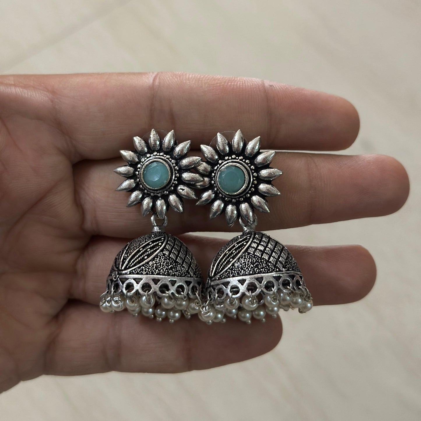 Oxidized silver jhumka earrings with sunflower studs, turquoise center, and pearl hangings.