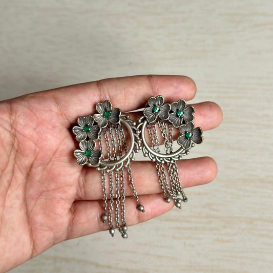 Oxidized floral earrings with green stone accents and hanging chain tassels.