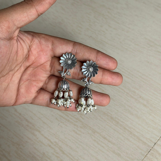 Pair of silver floral jhumka earrings with white pearl beads hanging.