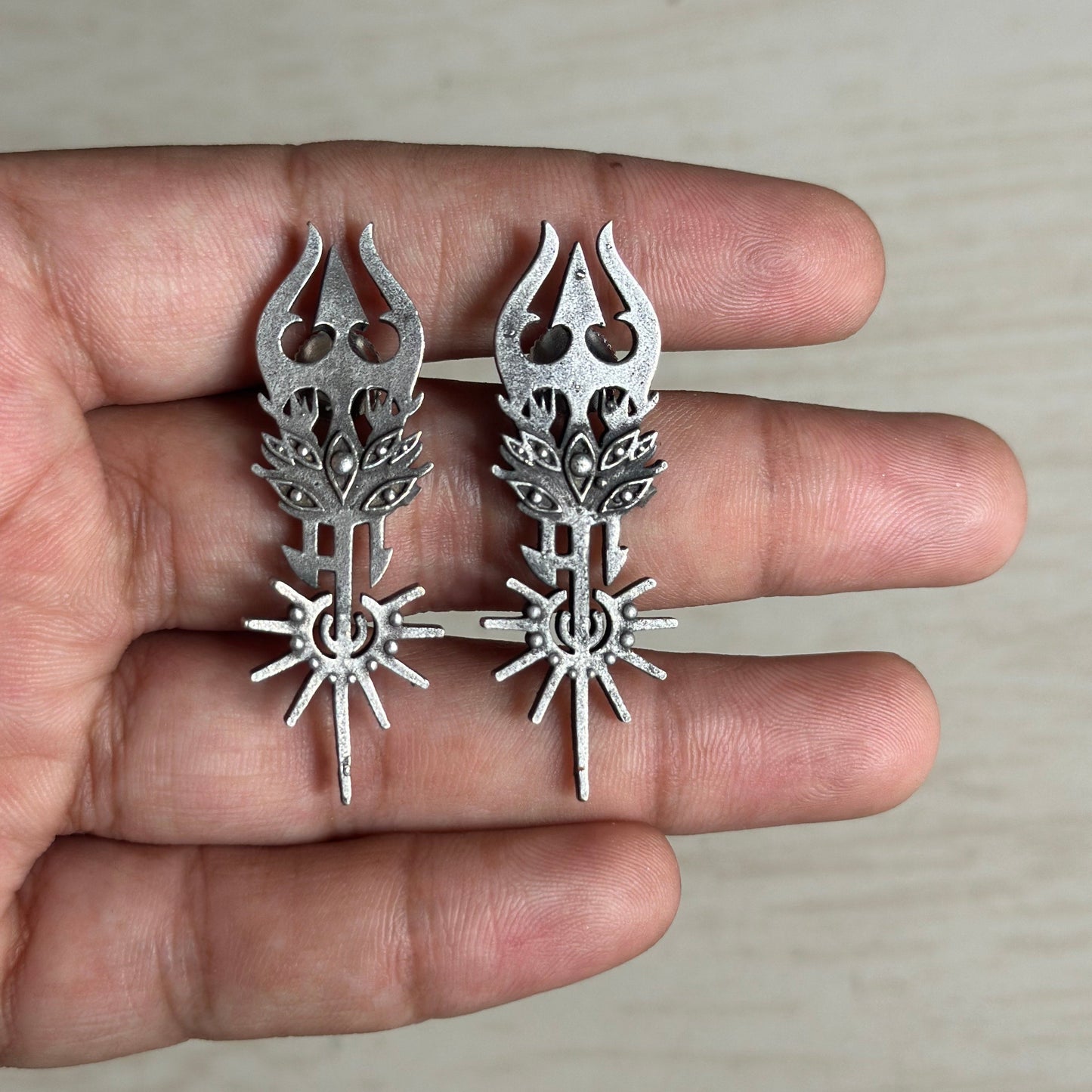 Oxidized silver earrings with a trident-inspired design and sunburst detailing.