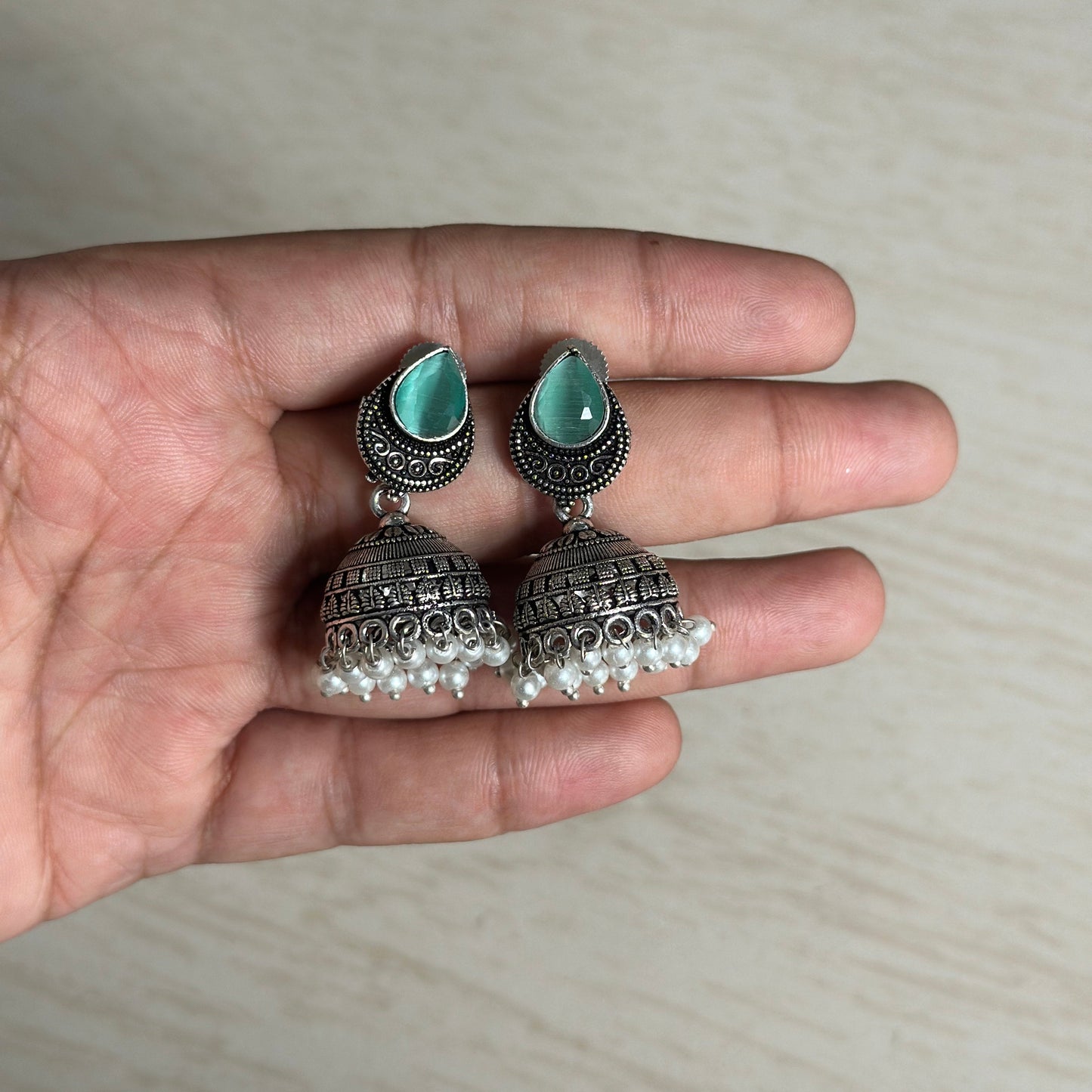 Oxidized silver jhumkas with green teardrop tops and pearl hangings.