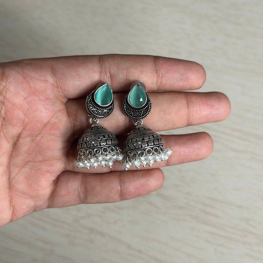 Oxidized silver jhumkas with green teardrop tops and pearl hangings.