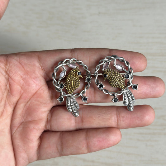 Oxidized silver earrings with golden peacocks inside a decorative floral circle.
