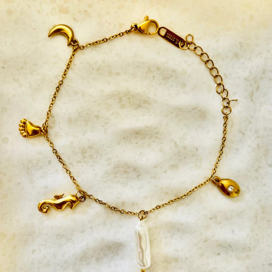gold charm bracelet featuring moon, footprint, seahorse, pearl, and teardrop motifs